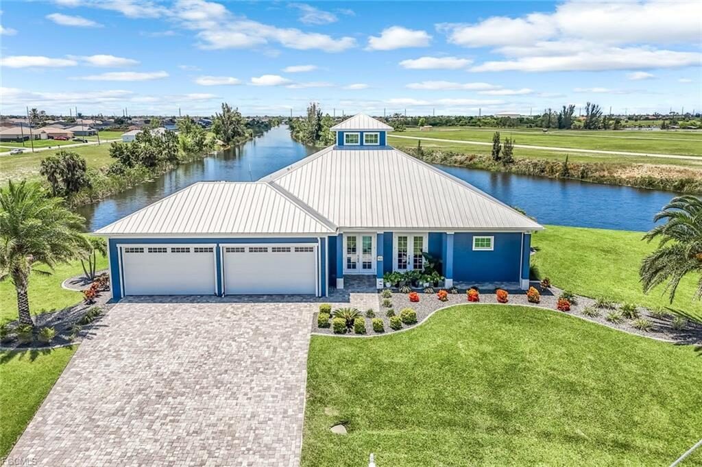 Lauren Homes coastal custom home with a silver metal roof, cupola, blue exterior, three-car garage and paver driveway on a Cape Coral canal