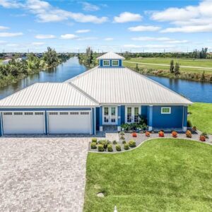 Lauren Homes coastal custom home with a silver metal roof, cupola, blue exterior, three-car garage and paver driveway on a Cape Coral canal
